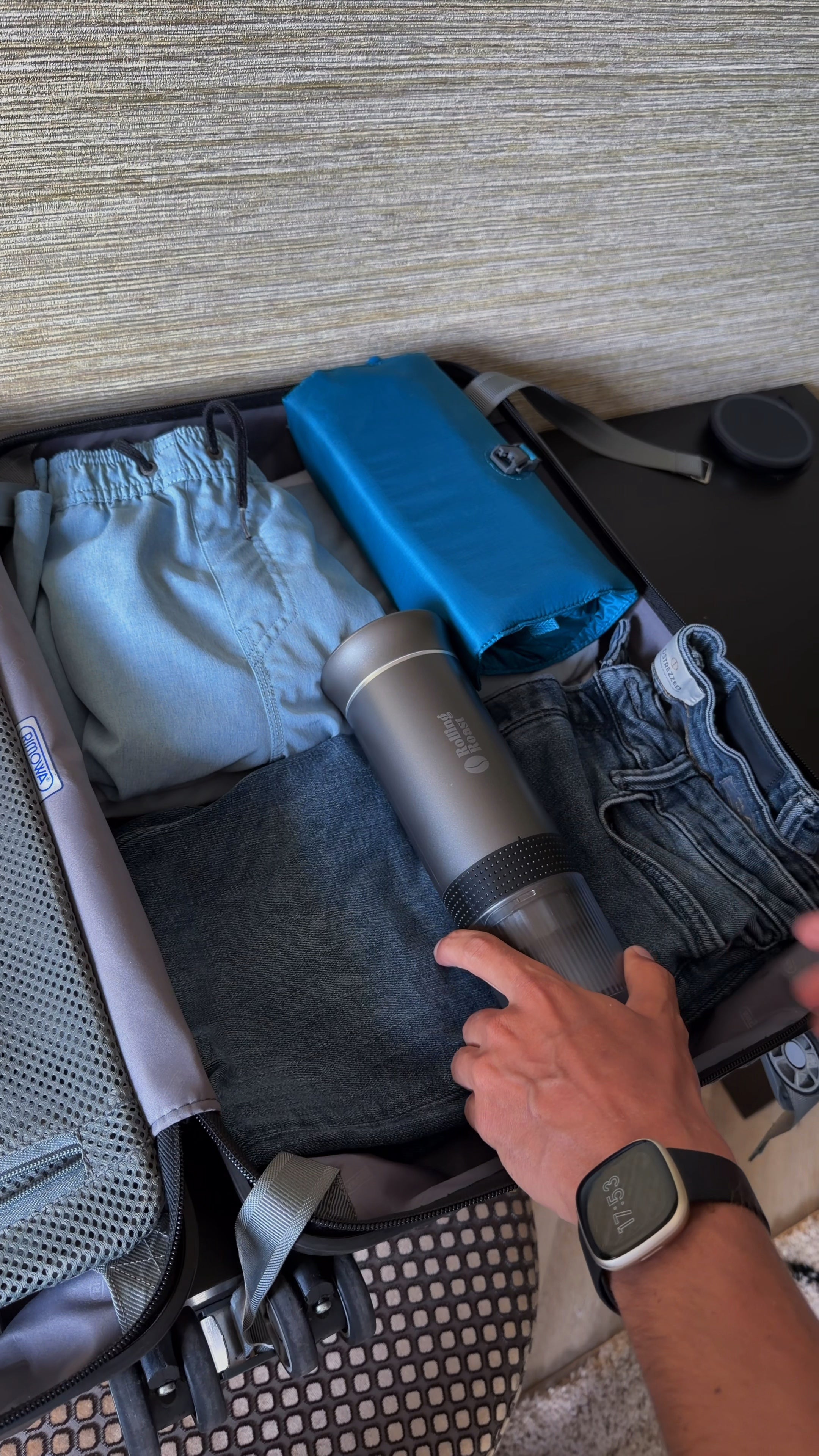Rolling Roast Nomad in zilver wordt in een reiskoffer gepakt tussen kleding, draagbare espressomachine voor onderweg
